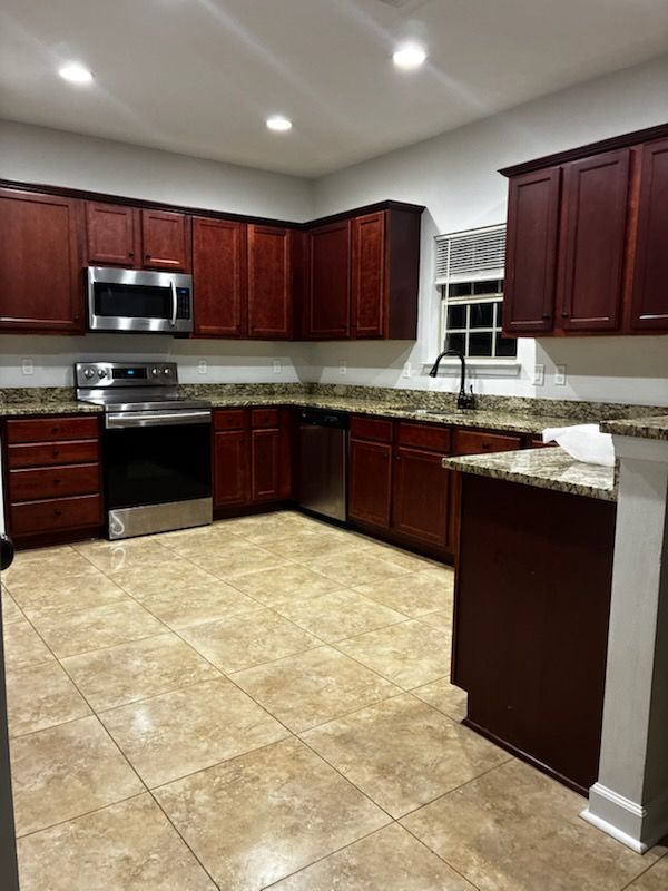 Kitchen with dark wood cabinets, stainless steel appliances, and beige tile floor.
