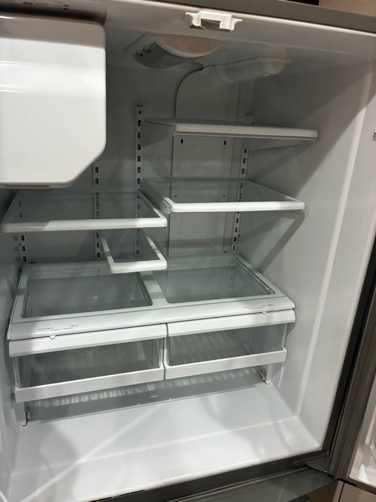 Empty refrigerator interior with glass shelves and drawers.