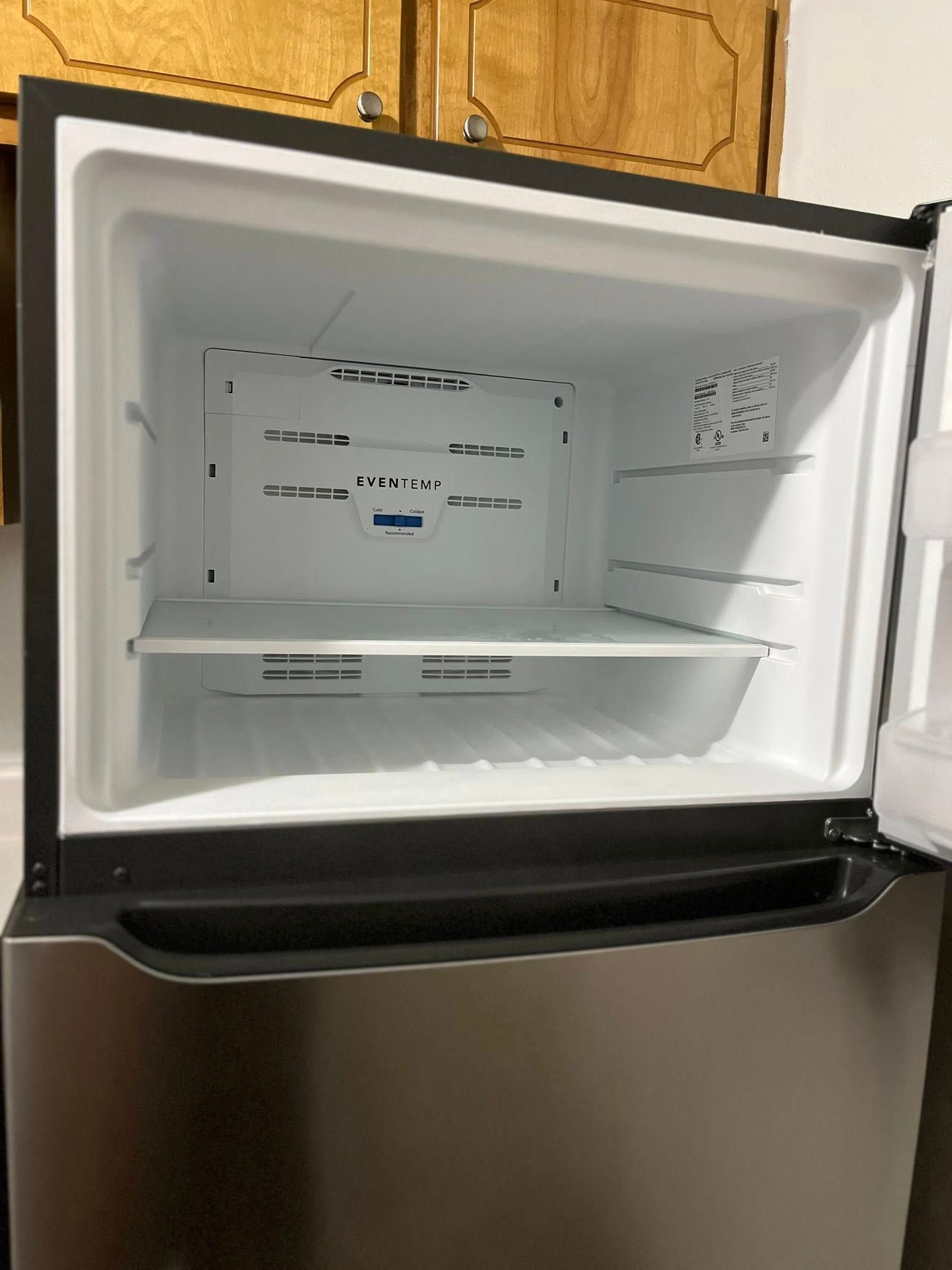 Open stainless steel refrigerator with an empty, white interior.