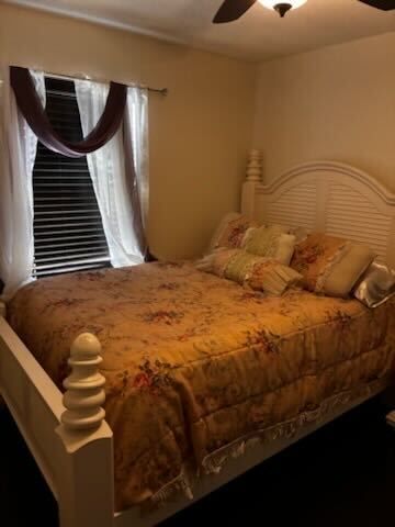 Cozy bedroom with a white bed, floral bedding, and a window with sheer curtains and dark drapes.