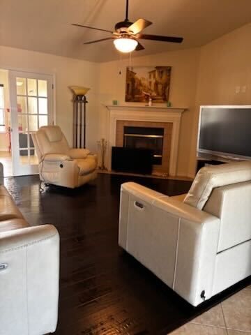 Living room with white leather chairs, dark wood floors, fireplace, ceiling fan, and TV
