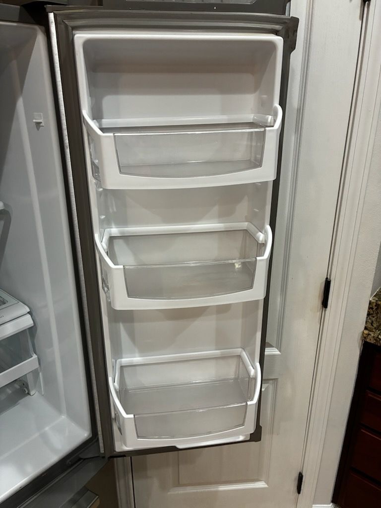 Open refrigerator door showing white freezer drawers and shelves inside.