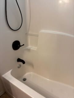 White bathtub and shower with black fixtures in a bathroom.