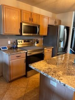 Modern kitchen with stainless appliances, wood cabinets, granite island, and tile floor.
