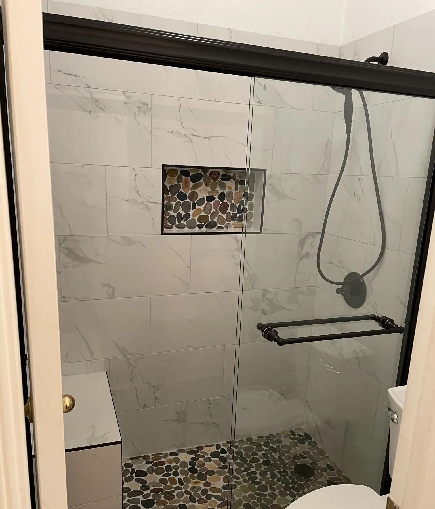 Glass shower with patterned tile accent, black shower rod, and built-in shelf in a bathroom.