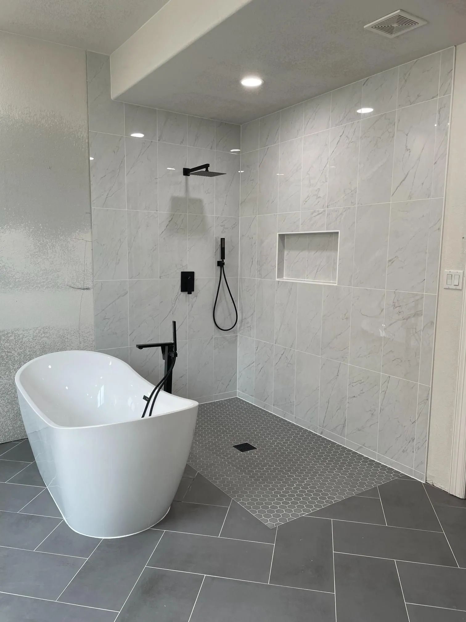 Modern bathroom with a white tub, walk-in shower, gray tile floor, and black fixtures.
