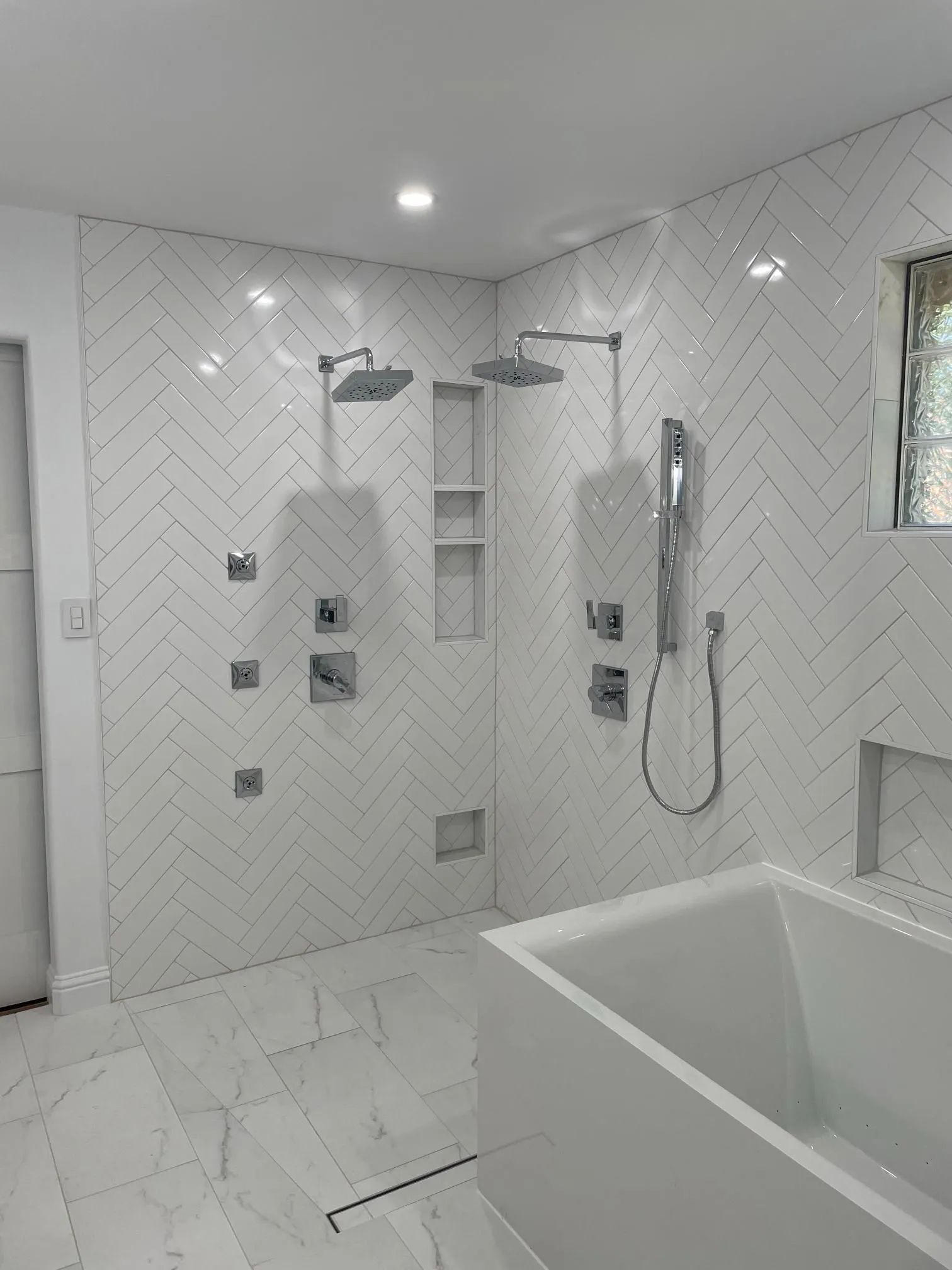 Modern white tiled bathroom with walk-in shower, ladder shelf, and bathtub edge visible