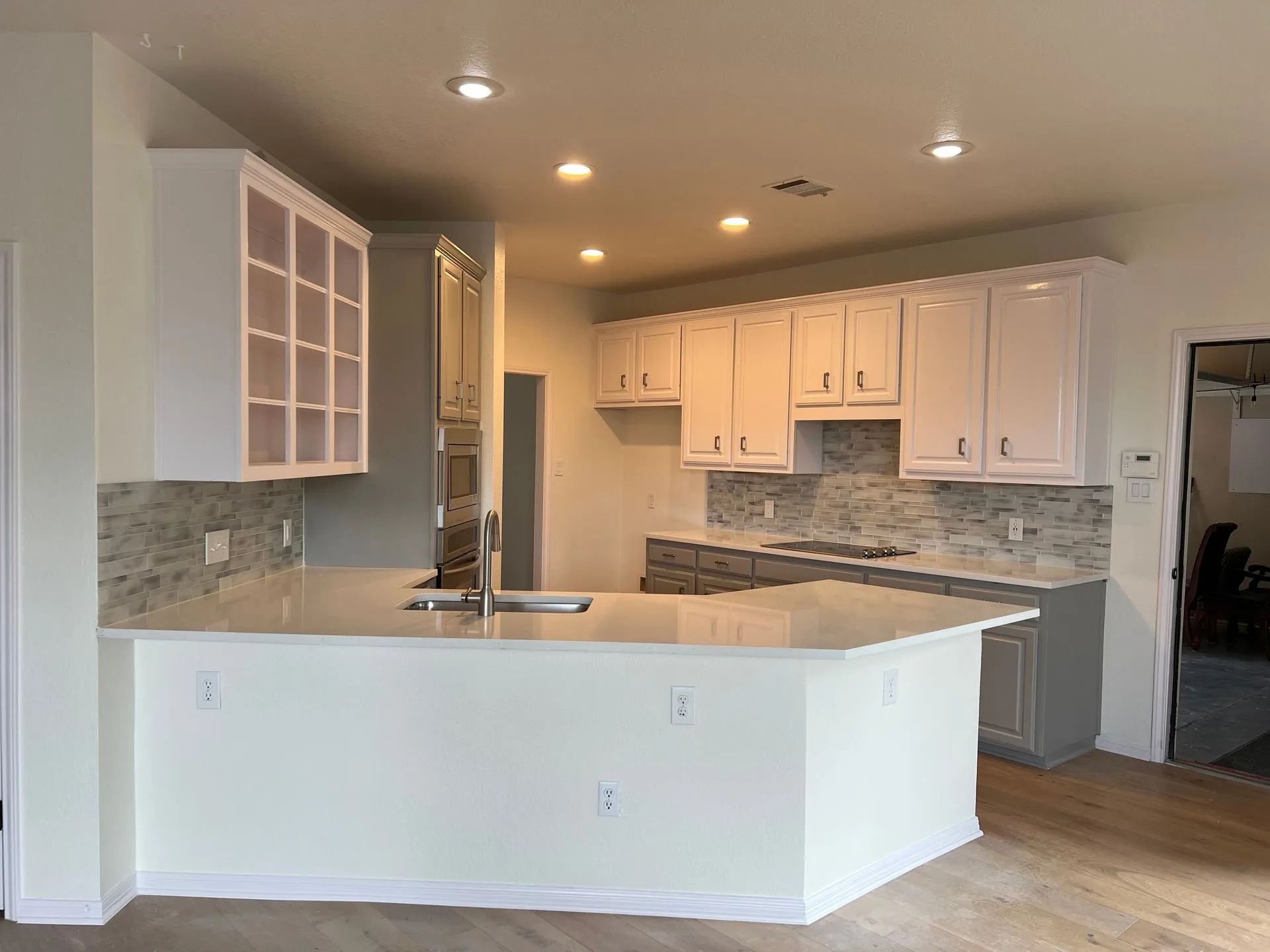 Open kitchen with white cabinets, gray tile backsplash, and a curved breakfast bar.