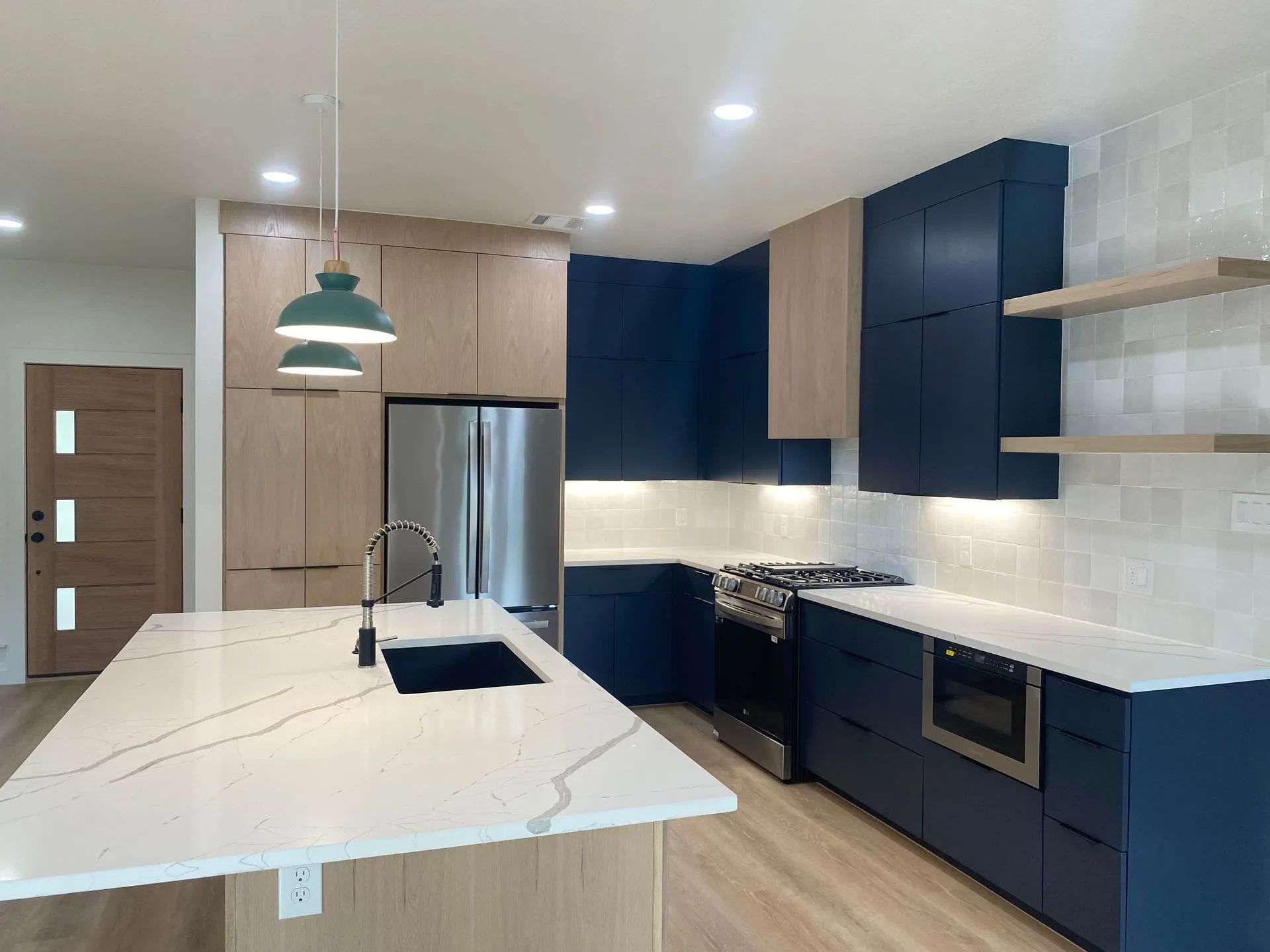 Modern kitchen with navy cabinets, white island, stainless appliances, and pendant lights