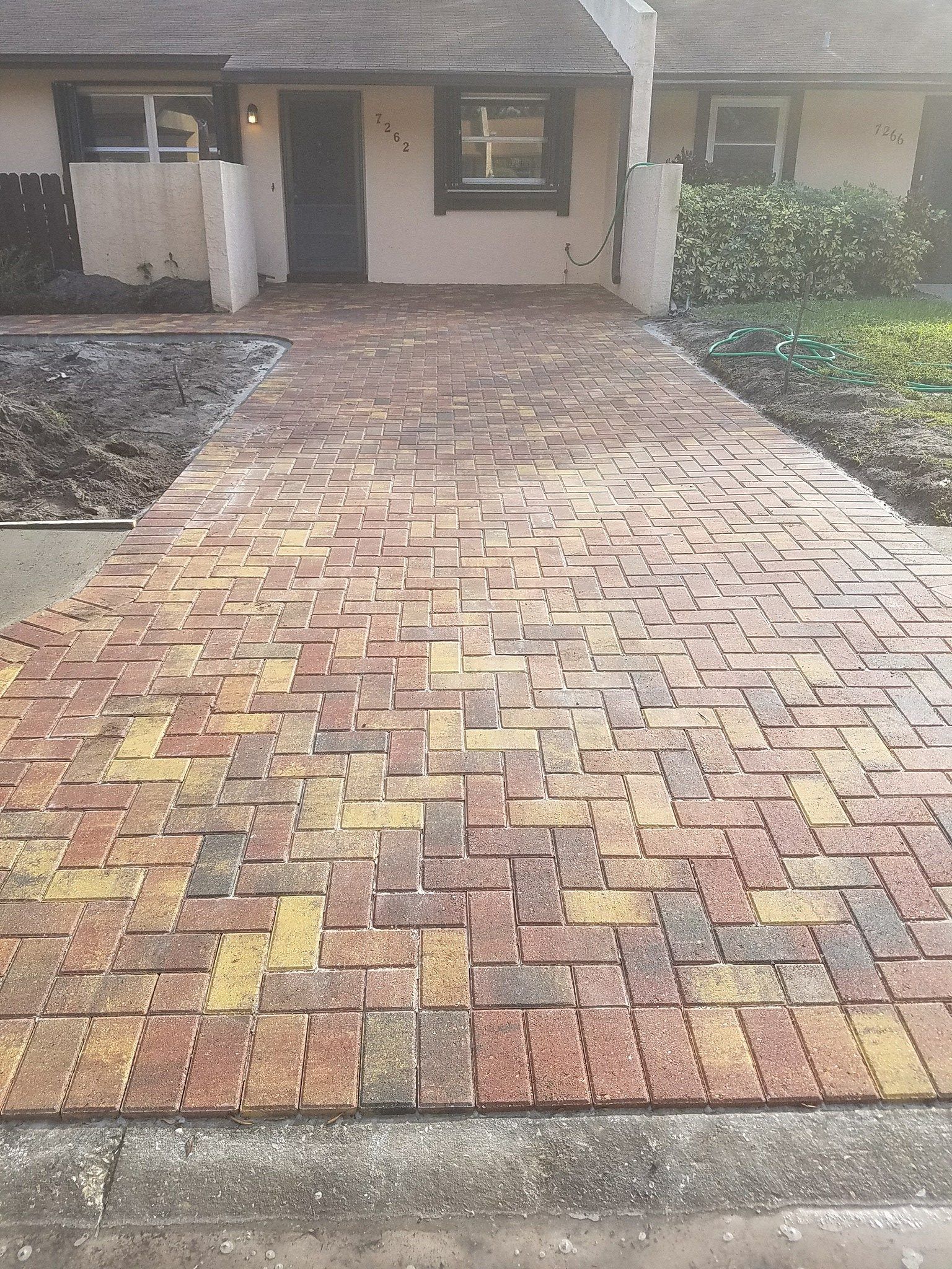Brick paved walkway leading to a house entrance. The bricks are red, yellow and brown.