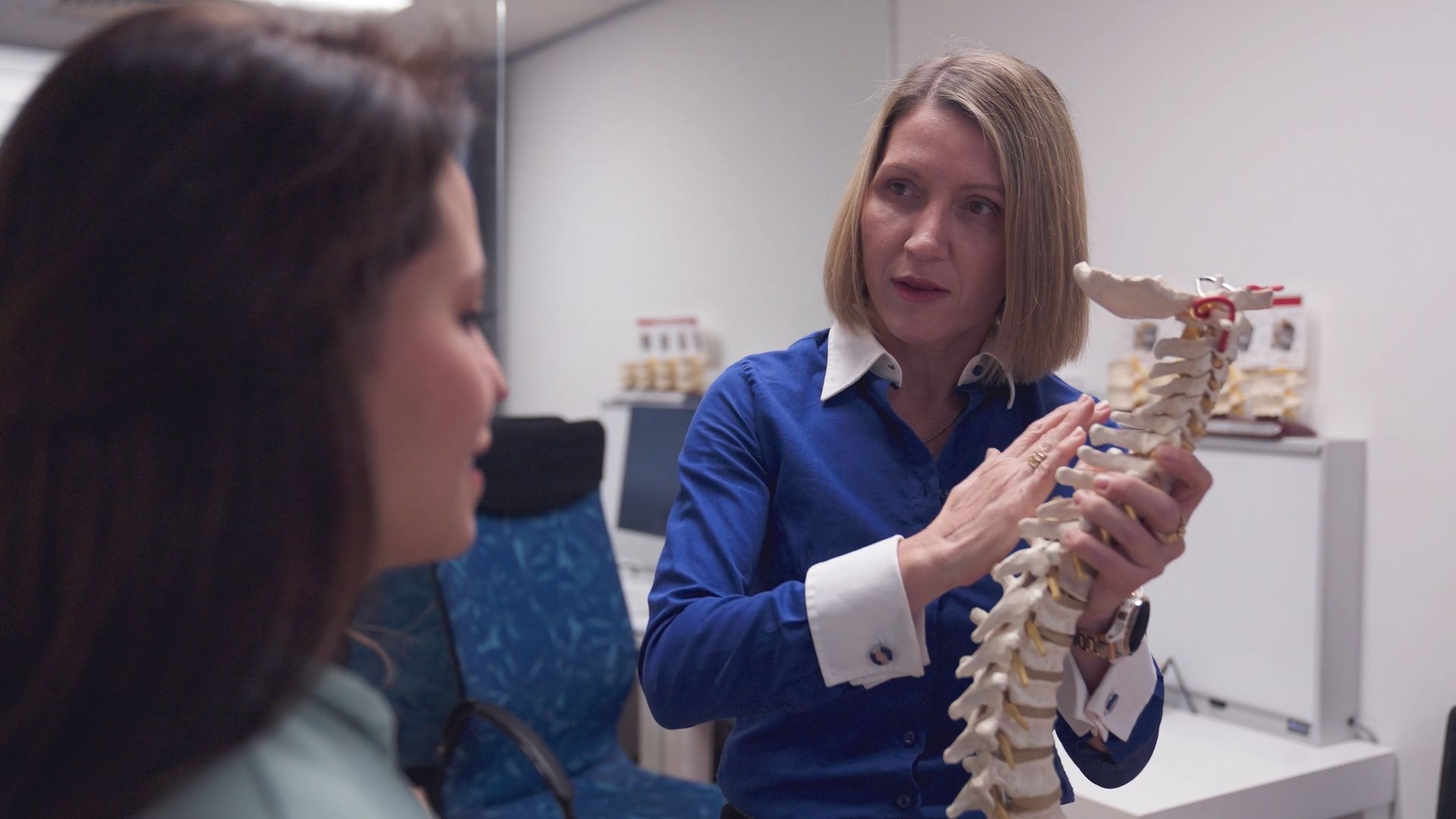 A woman is holding a model of a spine while talking to another woman.