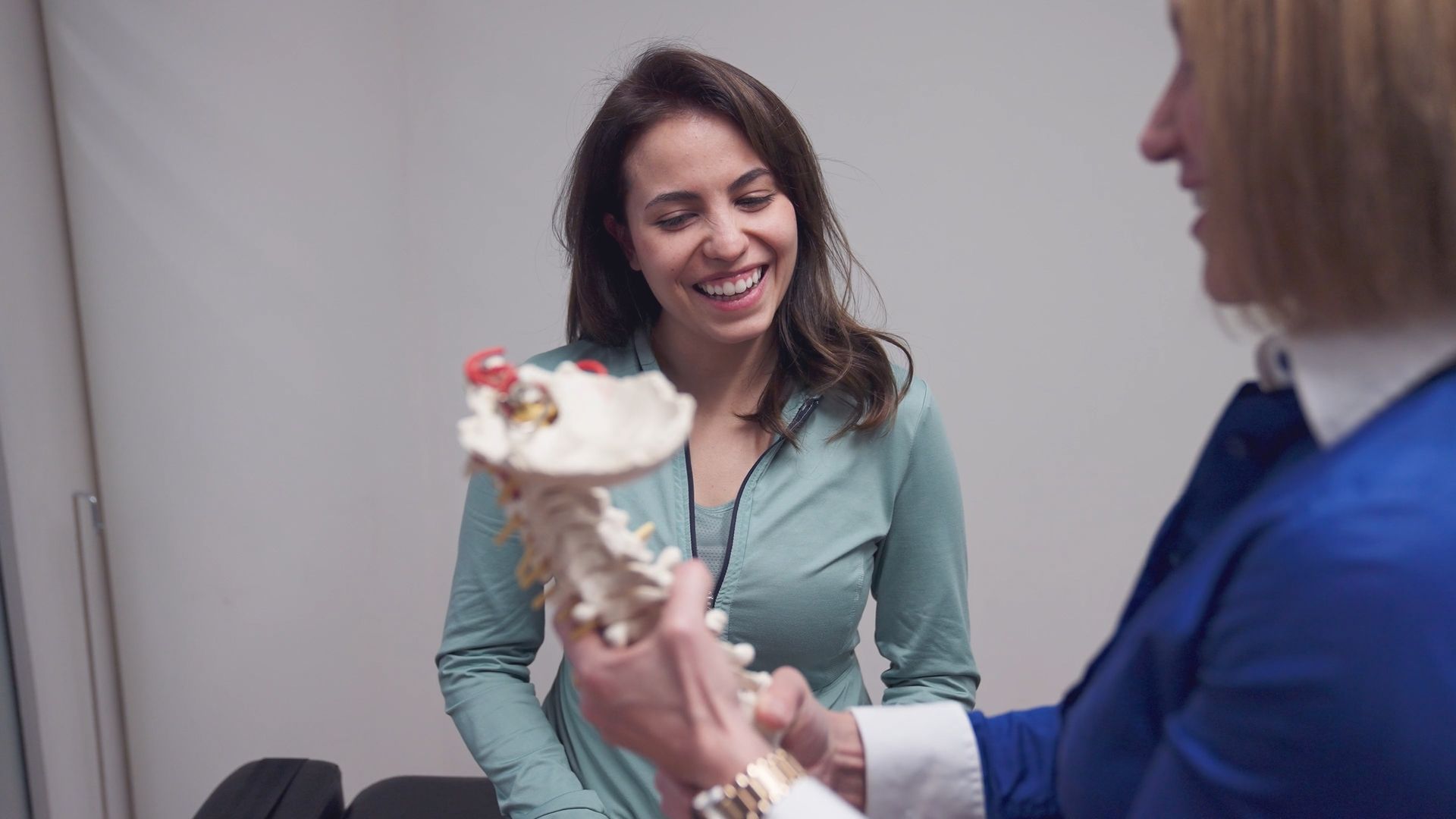 A woman is smiling while explaining a model of a spine.