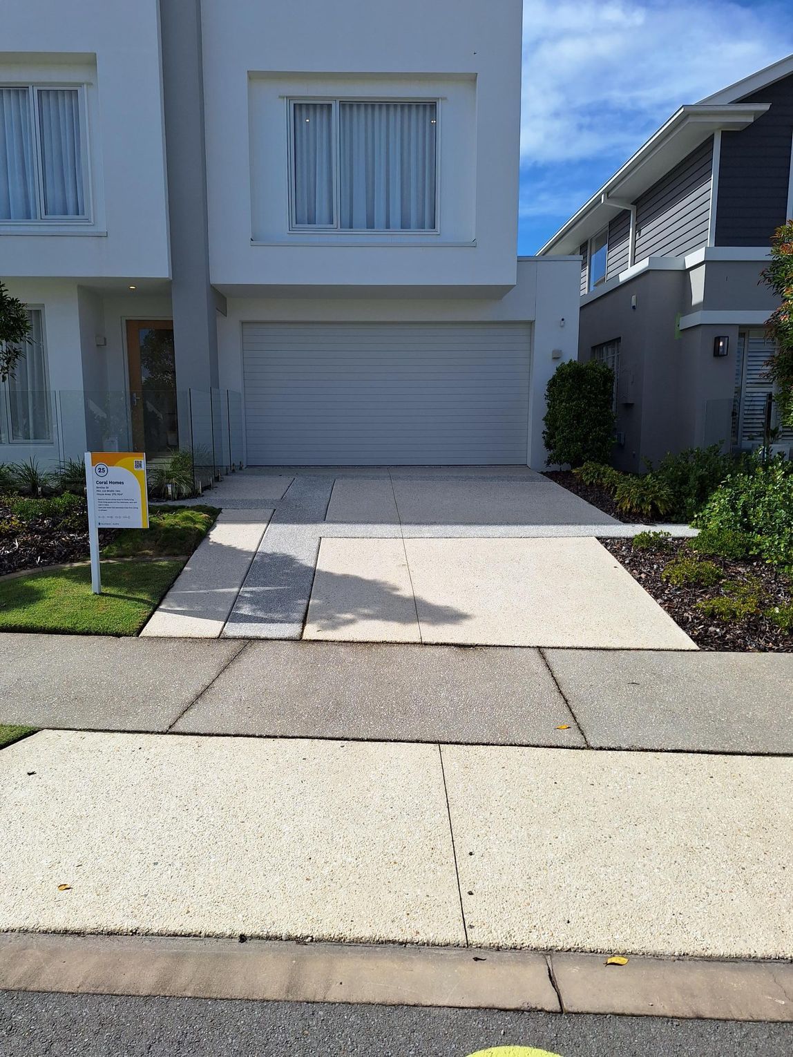 Driveway leading to a white house with a garage, flanked by a sidewalk and landscaping under a blue sky — DPC Decorative Patterned Concrete in Sunrise Beach, QLD