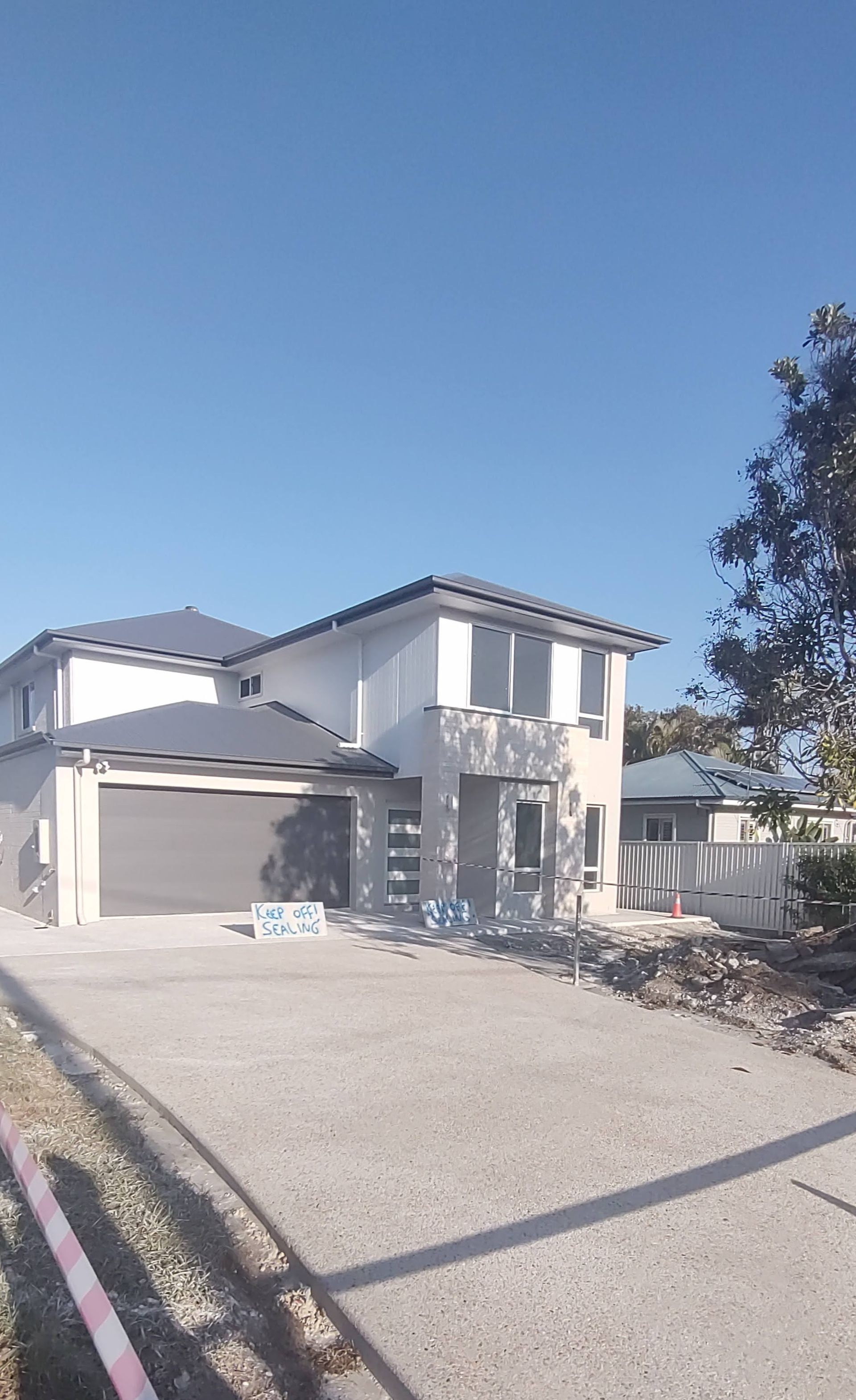 Two-story house under construction with a gray garage door and gravel driveway under a clear blue sky