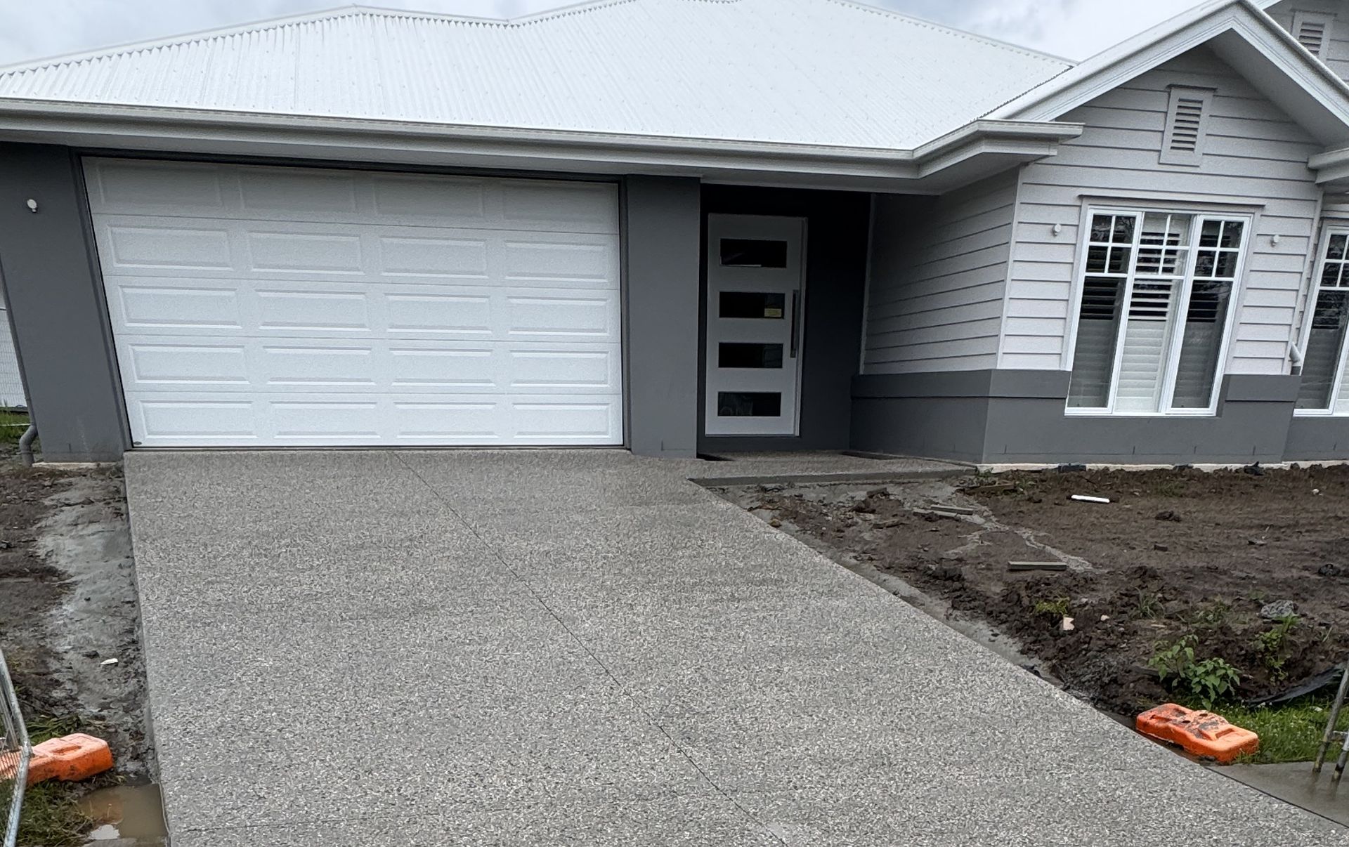 Front of a modern two-story house with a driveway. White exterior, closed garage door, and sidewalk in front — DPC Decorative Patterned Concrete in Sunrise Beach, QLD