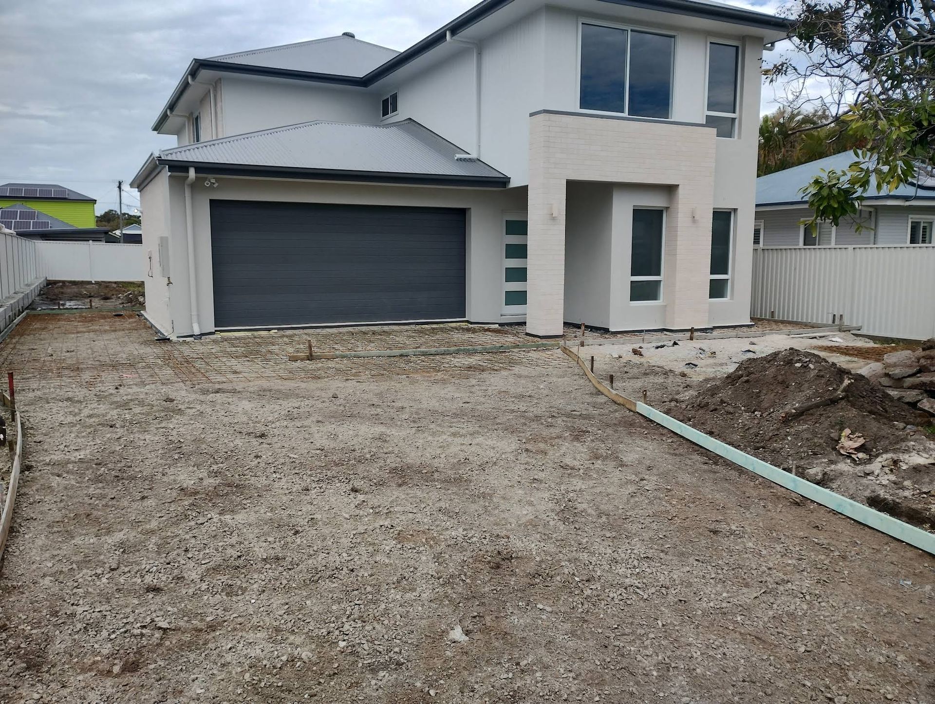 House With Garage Door, Gravel Driveway, and Construction Materials — DPC Decorative Patterned Concrete in Maroochydore, QLD