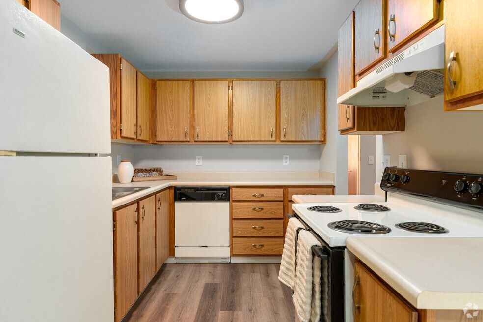 A kitchen with a stove , refrigerator , dishwasher , and wooden cabinets.