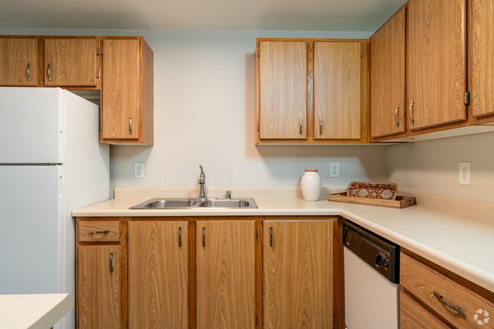 A kitchen with wooden cabinets , a sink , a refrigerator , and a dishwasher.