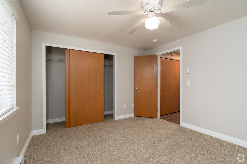 An empty bedroom with two closets and a ceiling fan.