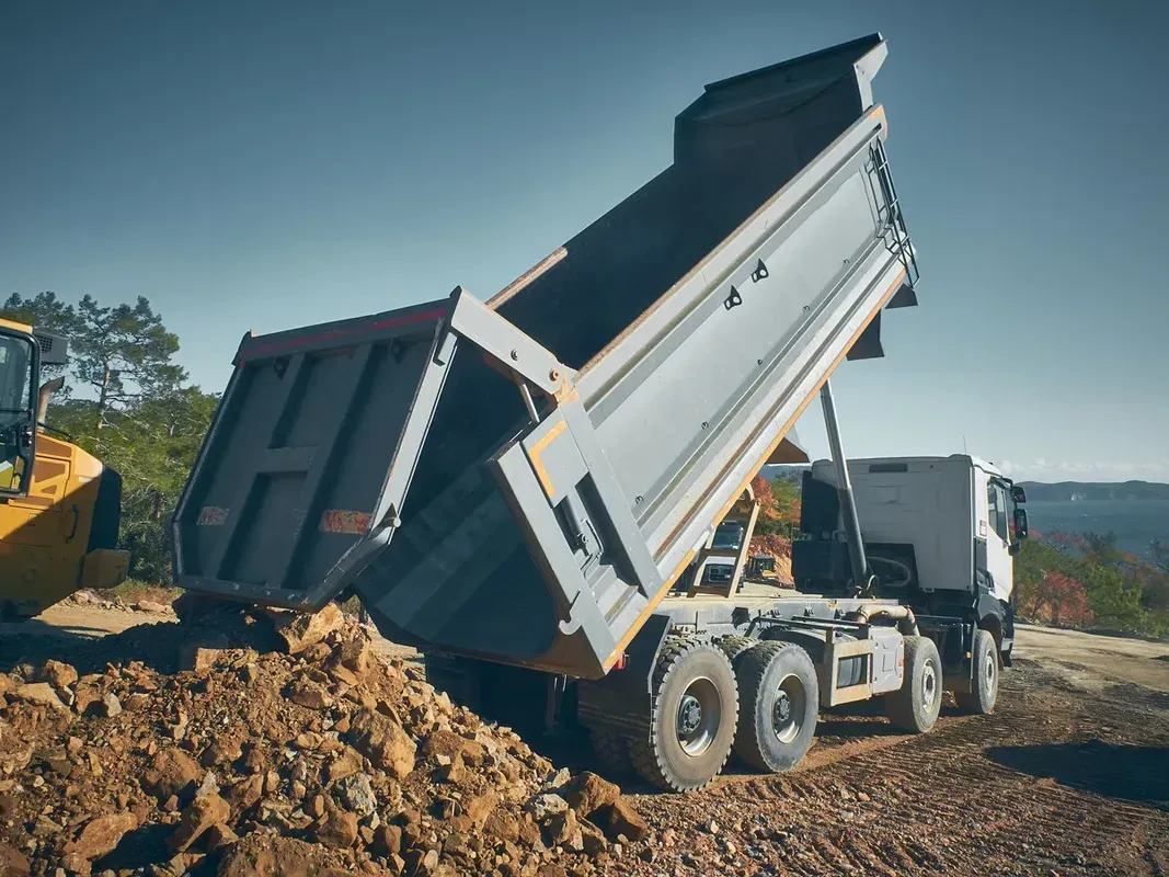 A White Dump Truck is Raised, Unloading a Pile of Soil and Rocks — Environment Restoration Solutions in Port Macquarie, NSW