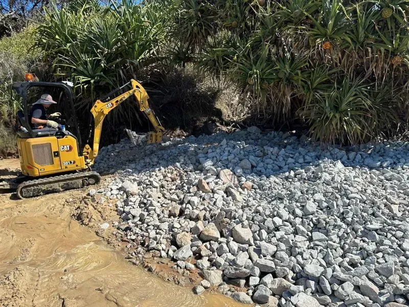 An Excavator Parked on Dirt Path Next to a Large Pile of Rocks — Environment Restoration Solutions in Waterview Heights, NSW