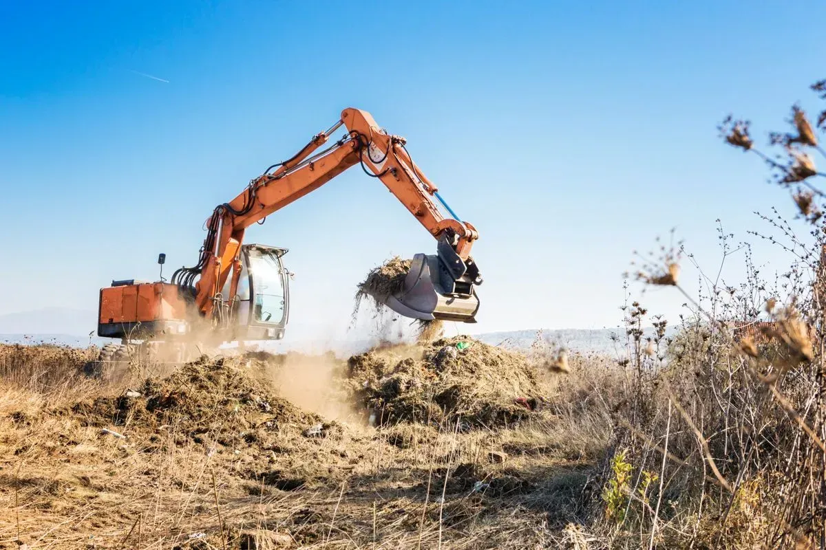 An Orange Excavator Digs Into a Dry, Dirt-covered Field — Environment Restoration Solutions in Waterview Heights, NSW