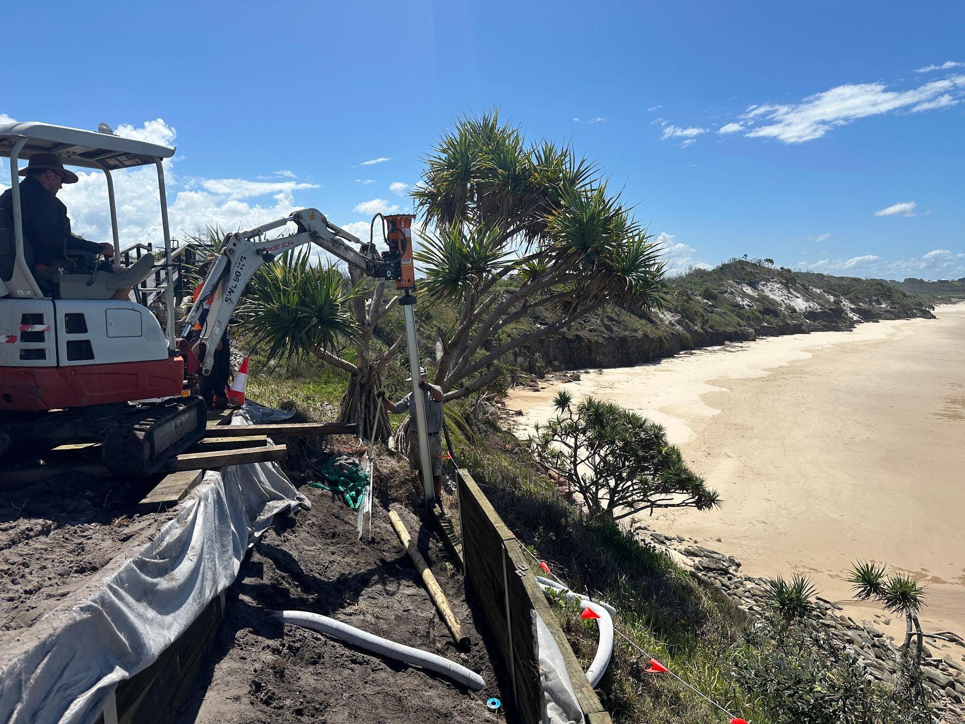 Excavator on A Sandy Beach Beside a Fence and Palm Trees Under a Clear Blue Sky — Environment Restoration Solutions in Waterview Heights, NSW