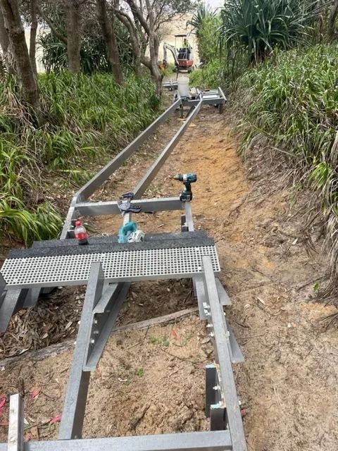 A Metal Track for a Funicular or Incline Lift Being Installed on a Sloped, Grassy Trail in a Wooded Area — Environment Restoration Solutions in Waterview Heights, NSW