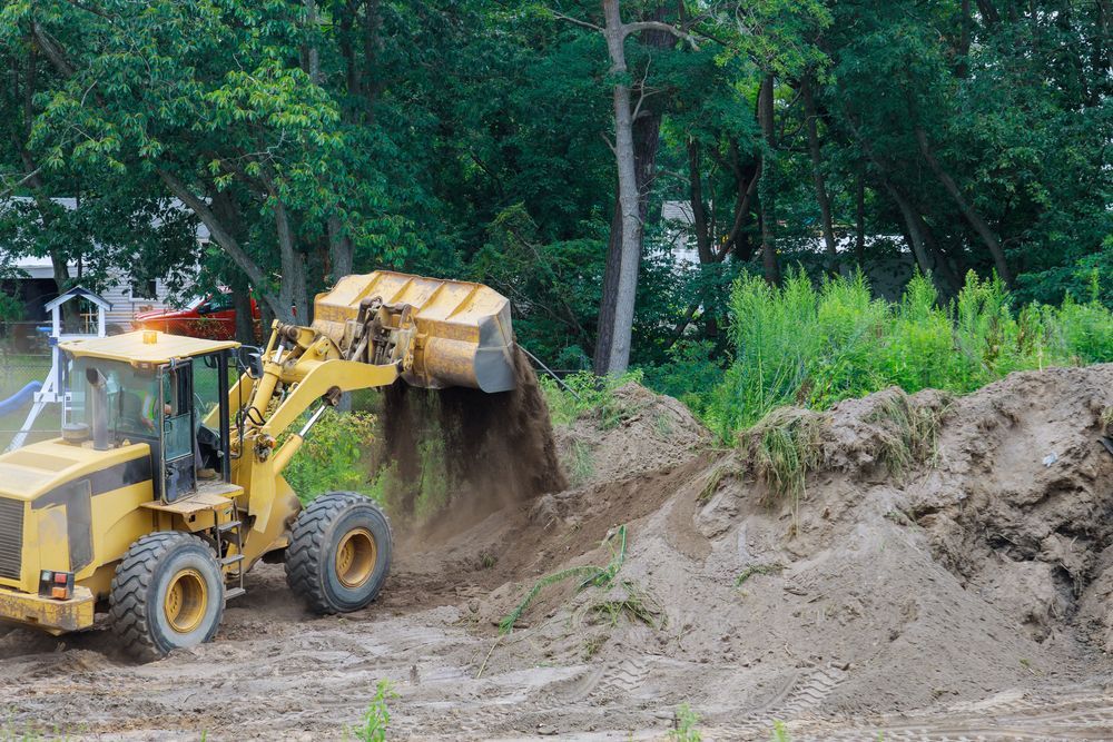Yellow Front Loader Dumping Soil on a Dirt Pile in a Wooded Construction Area — Environment Restoration Solutions in Waterview Heights, NSW