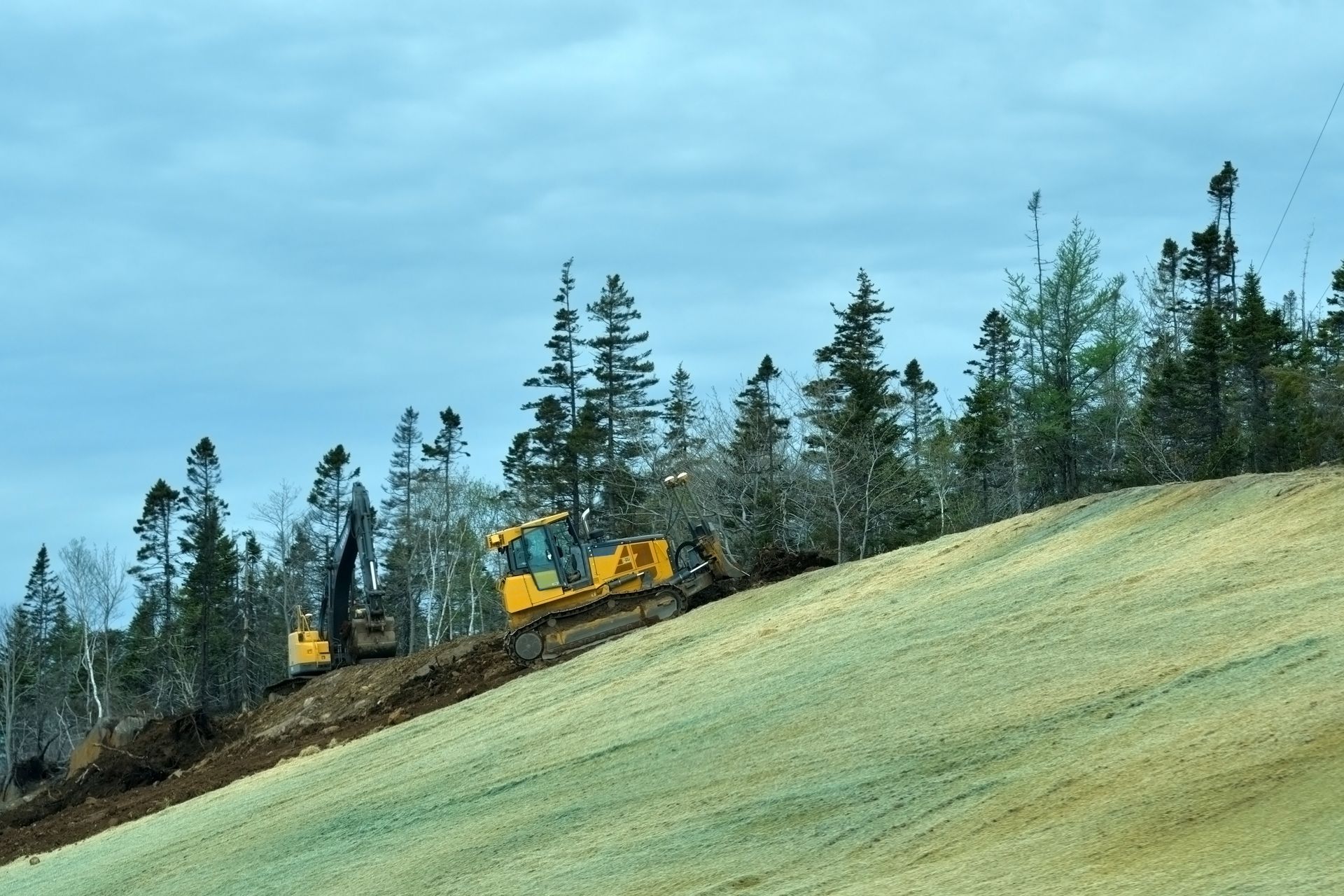 Yellow Heavy Construction Equipment Operates on a Grassy Hillside — Environment Restoration Solutions in Lismore, NSW