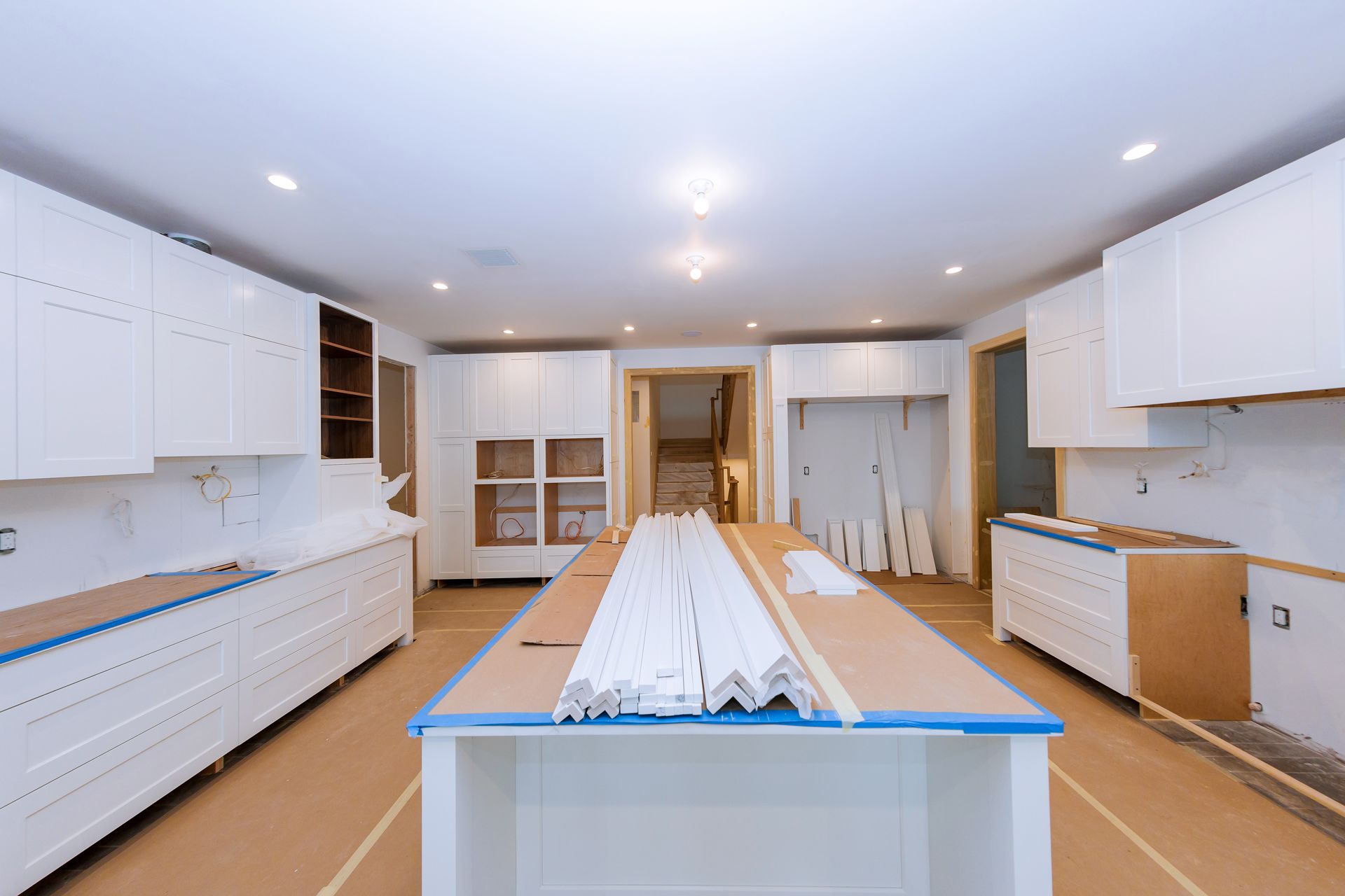 Kitchen renovation in progress, white cabinets installed, island with molding, unfinished.
