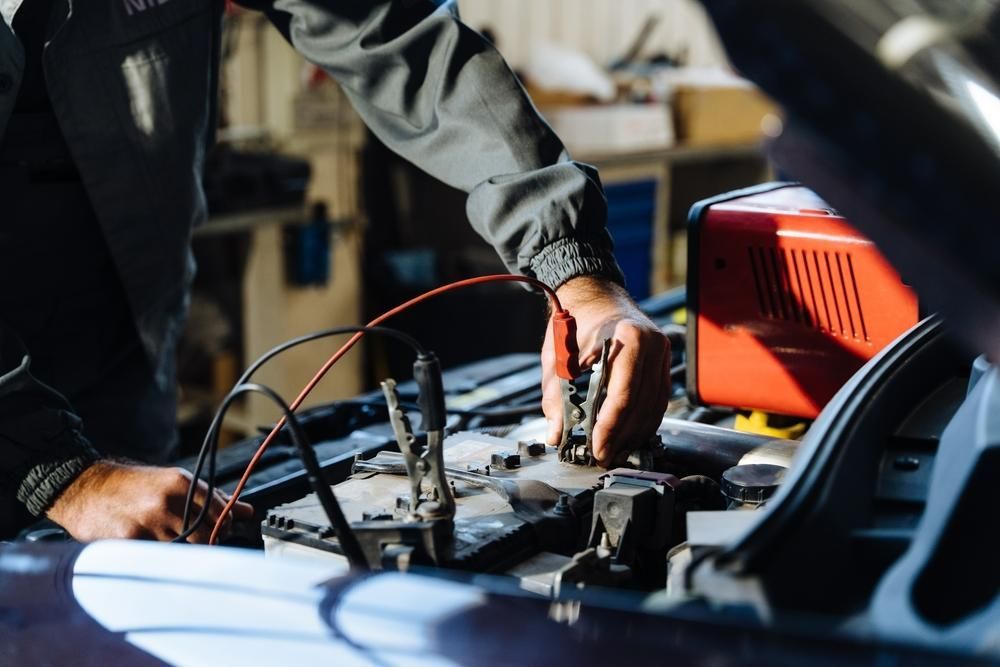 A Man Is Charging a Car Battery with A Charger — Belmont Auto Electrics and Air Conditioning in Belmont, NSW