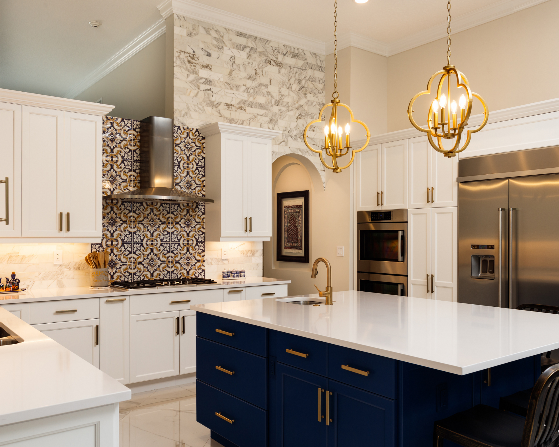 Elegant kitchen with white cabinets, blue island, gold fixtures, and patterned backsplash.