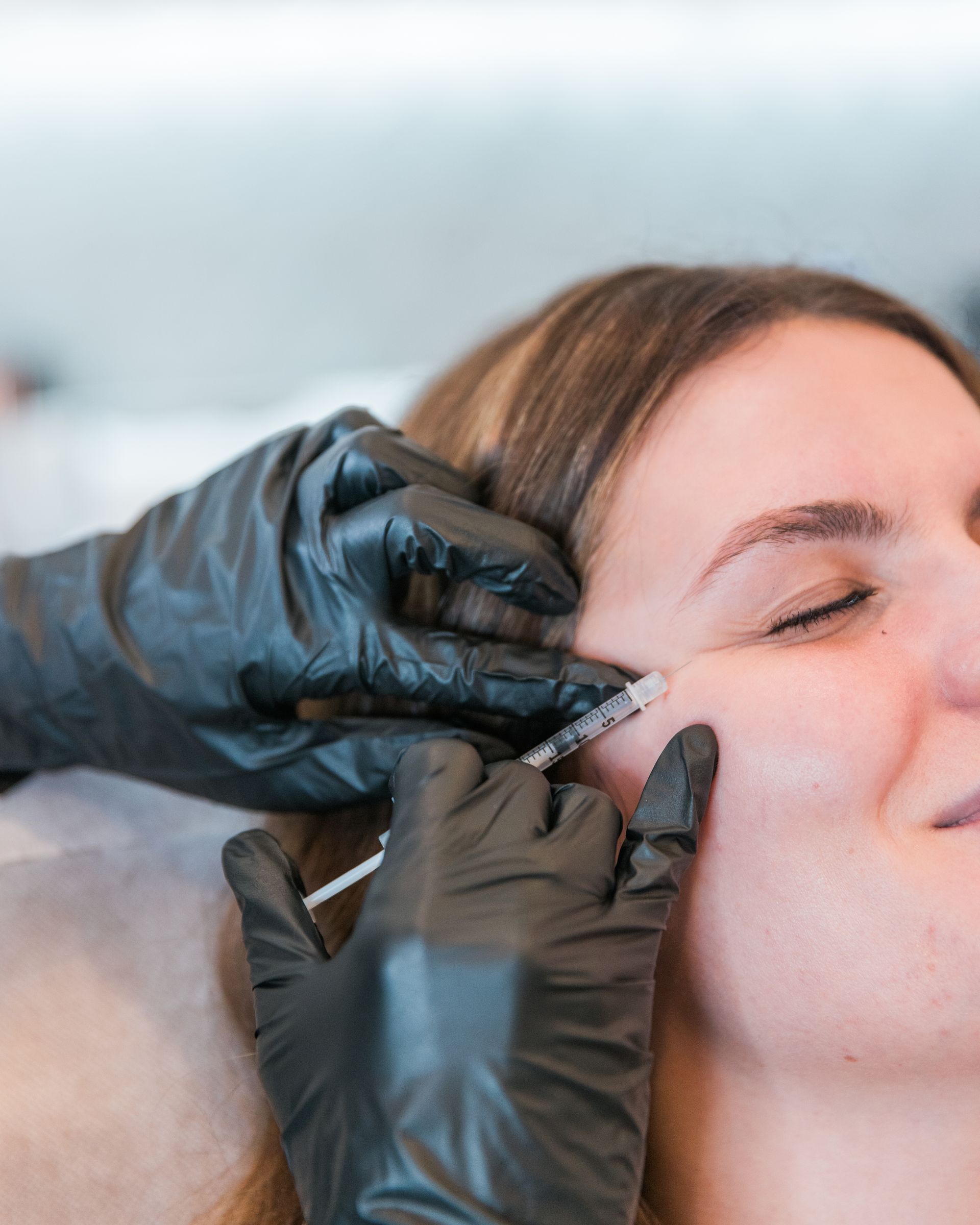 Gloved hands applying an eyebrow treatment to a woman’s face in a spa setting
