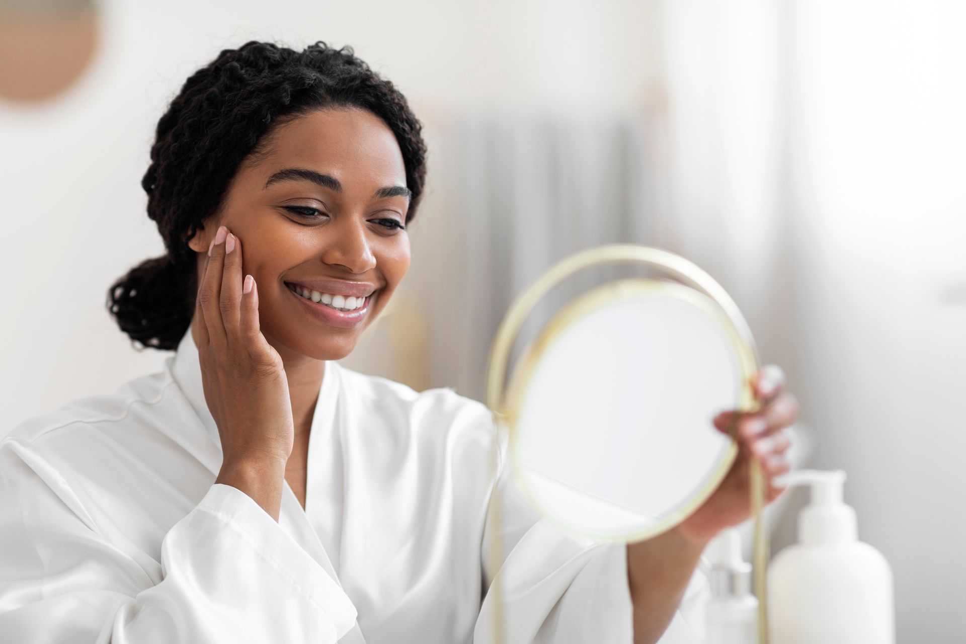 A woman is smiling while looking at her face in a mirror.