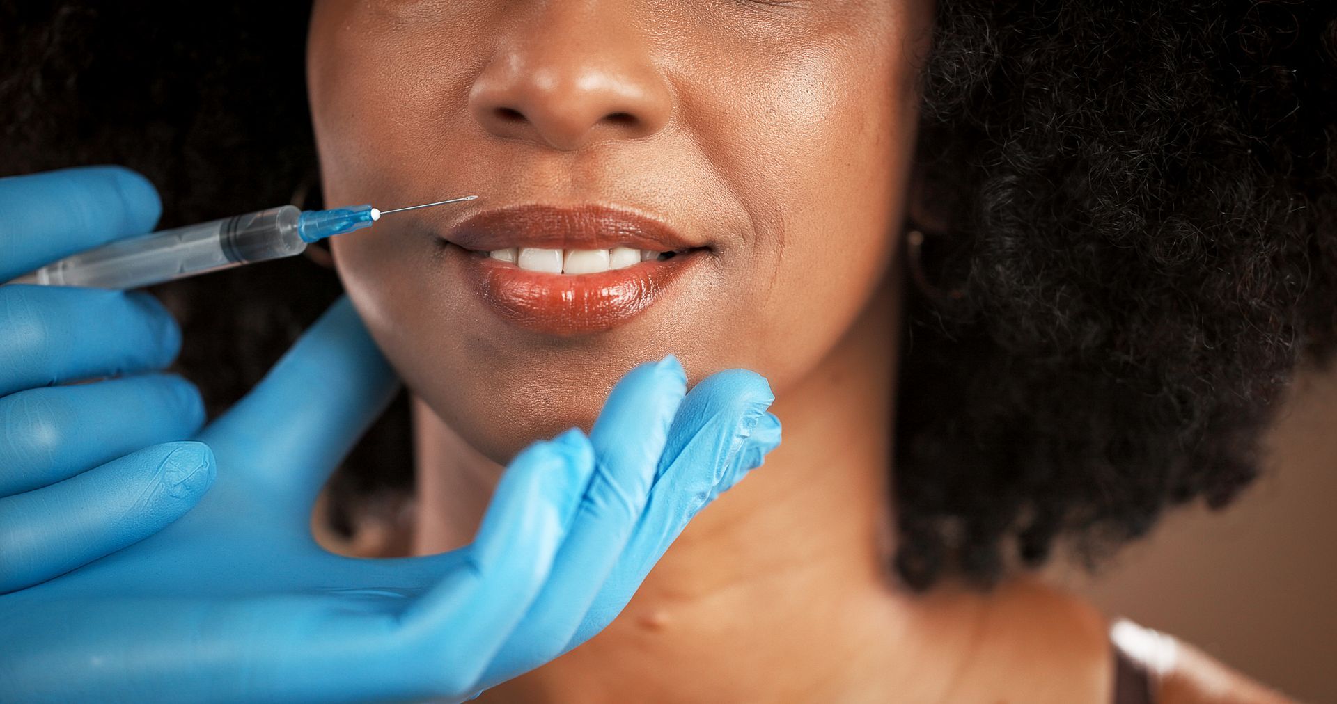 Woman receiving lip filler injection from gloved clinician in a close-up medical procedure