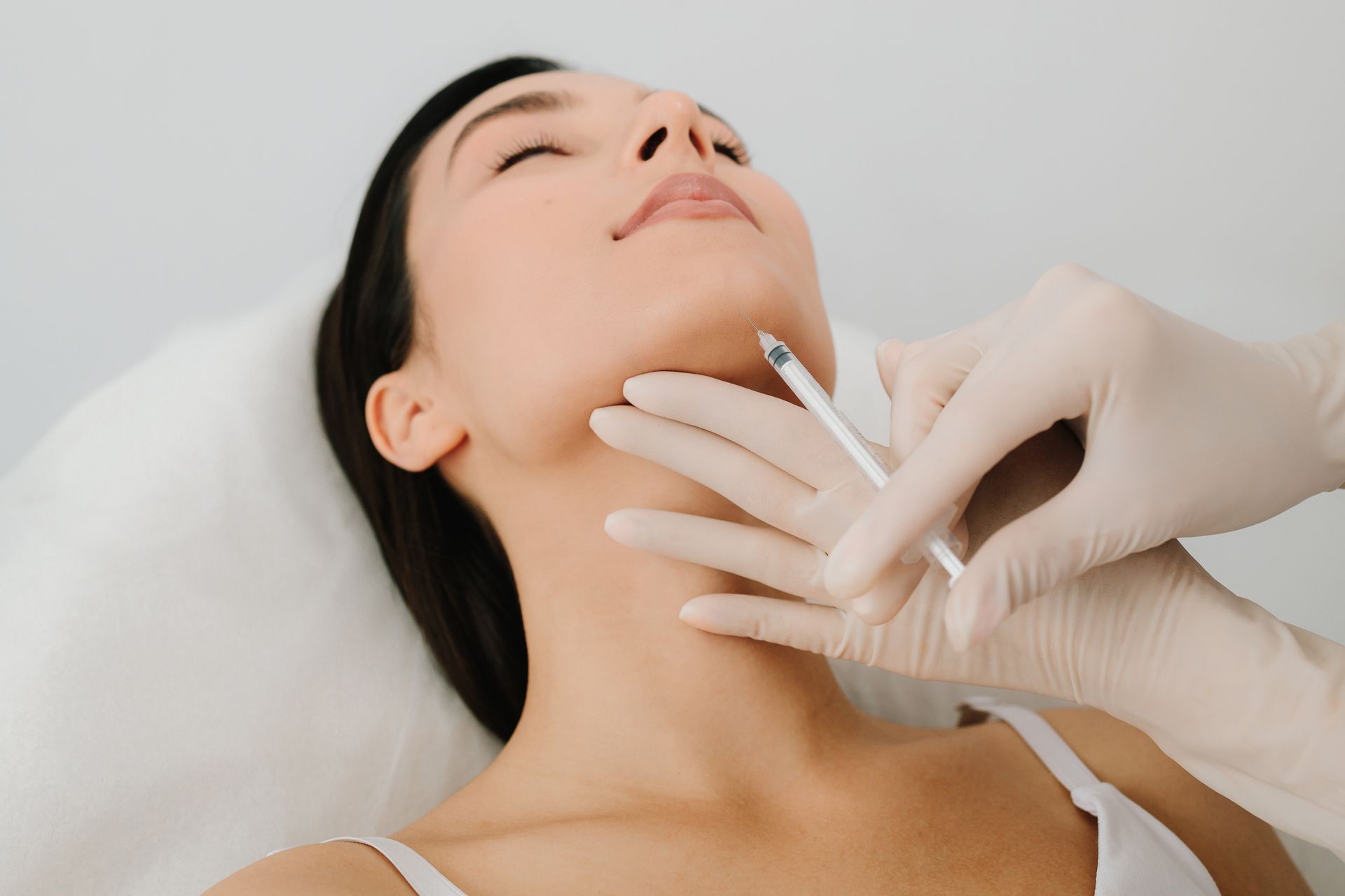 Gloved clinician injecting a woman’s neck in a medical procedure