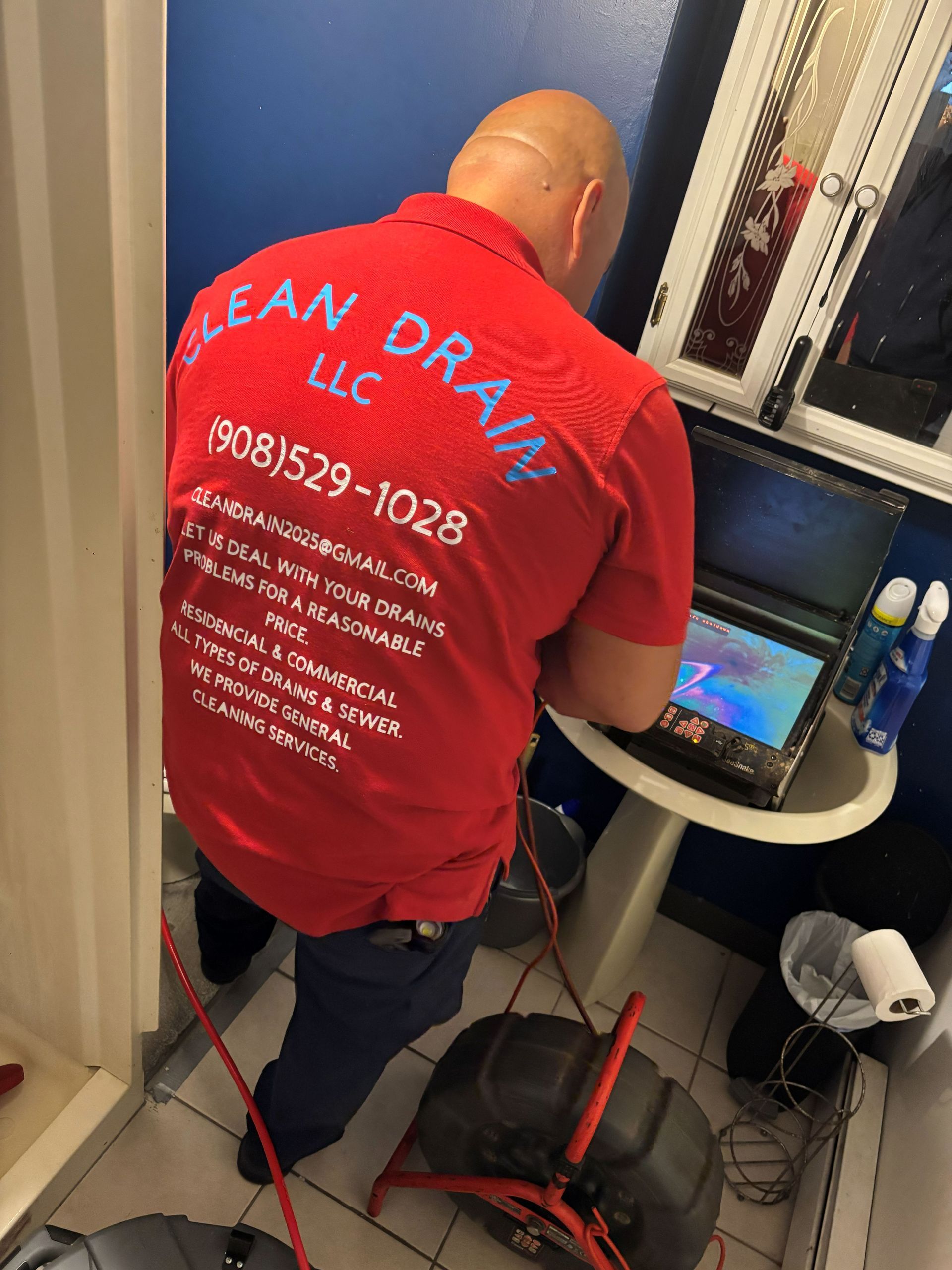 Technician in red shirt working on a laptop beside cables and equipment in a narrow room