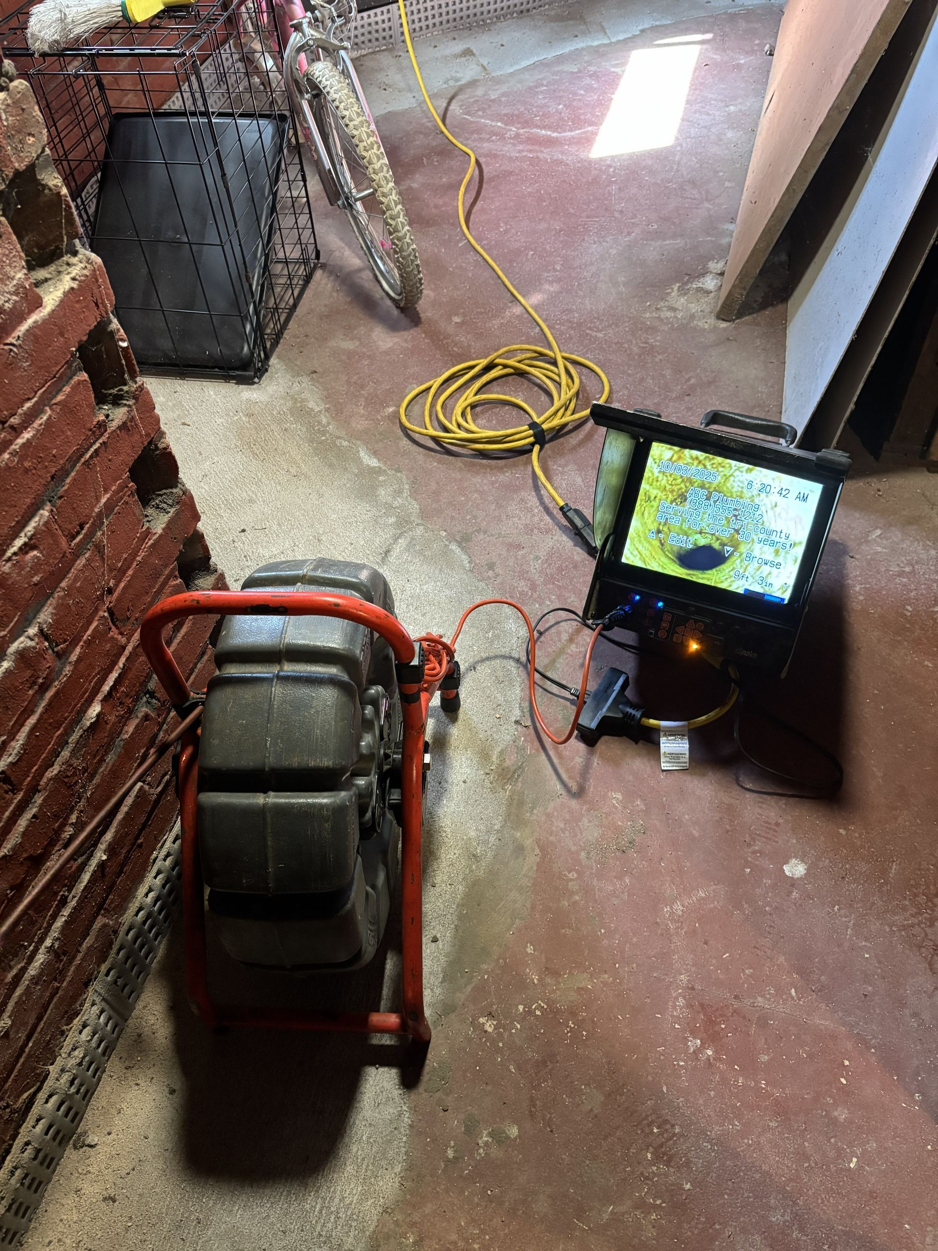 Red floor-cleaning machine beside a laptop showing a map in a hallway, with a coiled yellow cord nearby.