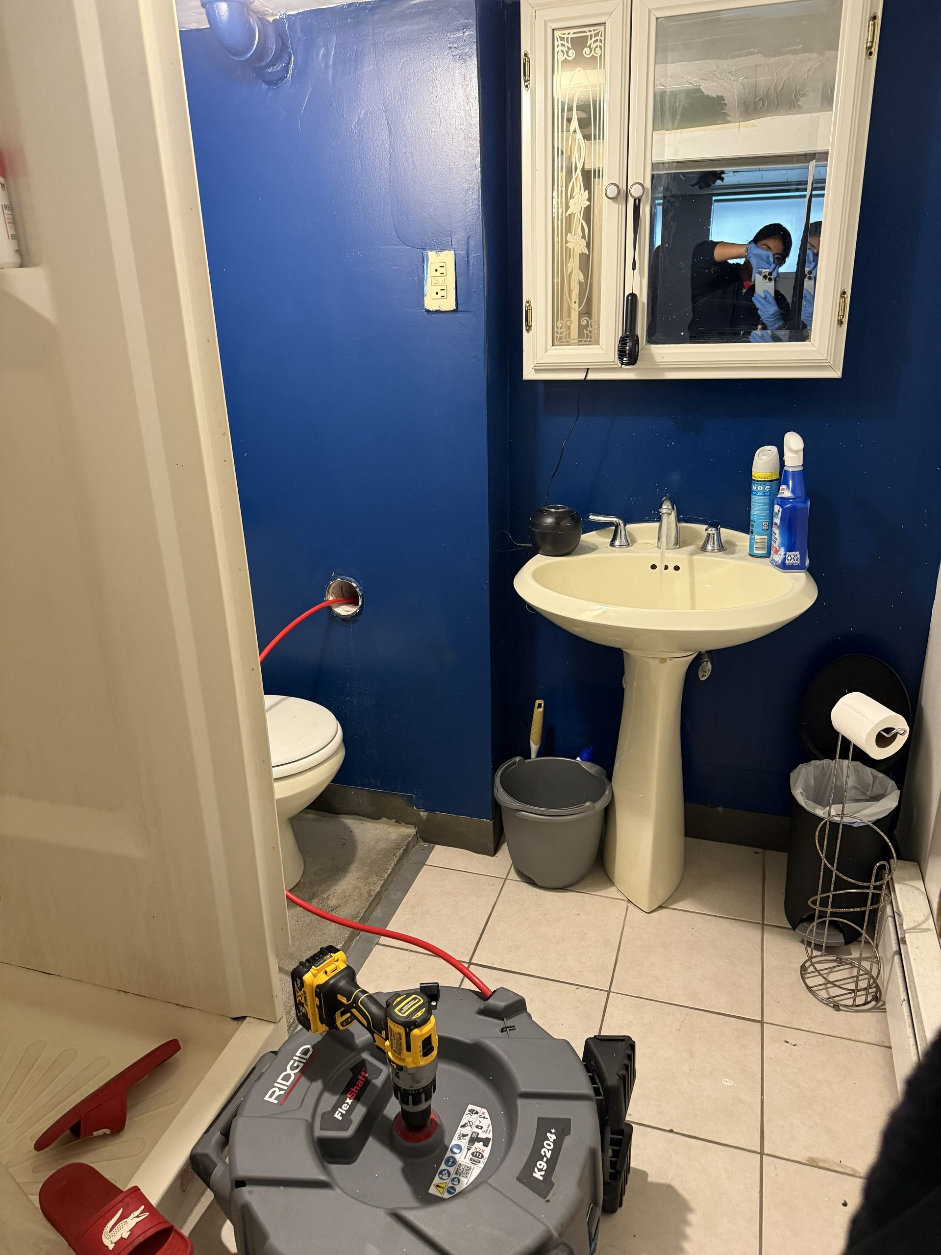 Small bathroom with blue wall, pedestal sink, toilet, mirror, and toys on the floor.