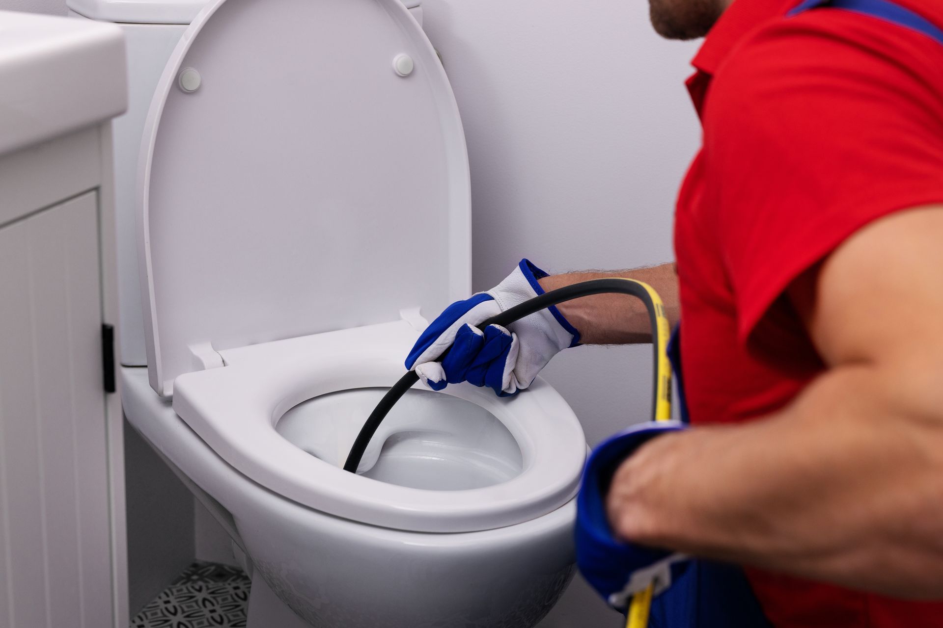 Person in red shirt cleaning a white toilet with blue gloves and cleaning tools