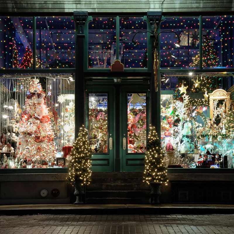 Festive storefront windows filled with Christmas trees and colorful holiday lights at night