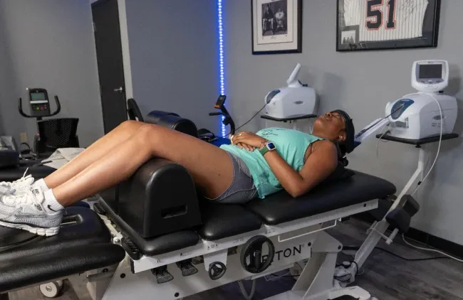 Person lying on a spinal decompression table in a clinic, with medical equipment nearby.