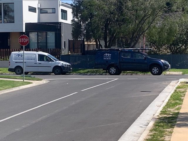 A man is sitting on a ladder fixing a light on the ceiling. White van and blue SUV at a street corner with a stop sign in a residential area.