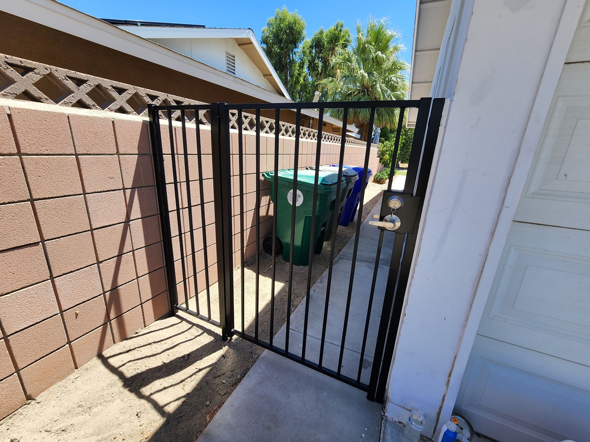 A black gate is open to a sidewalk next to a brick wall.