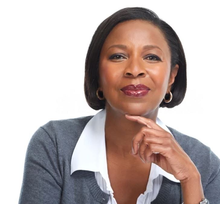 A woman wearing a gray sweater and white shirt has her hand on her chin