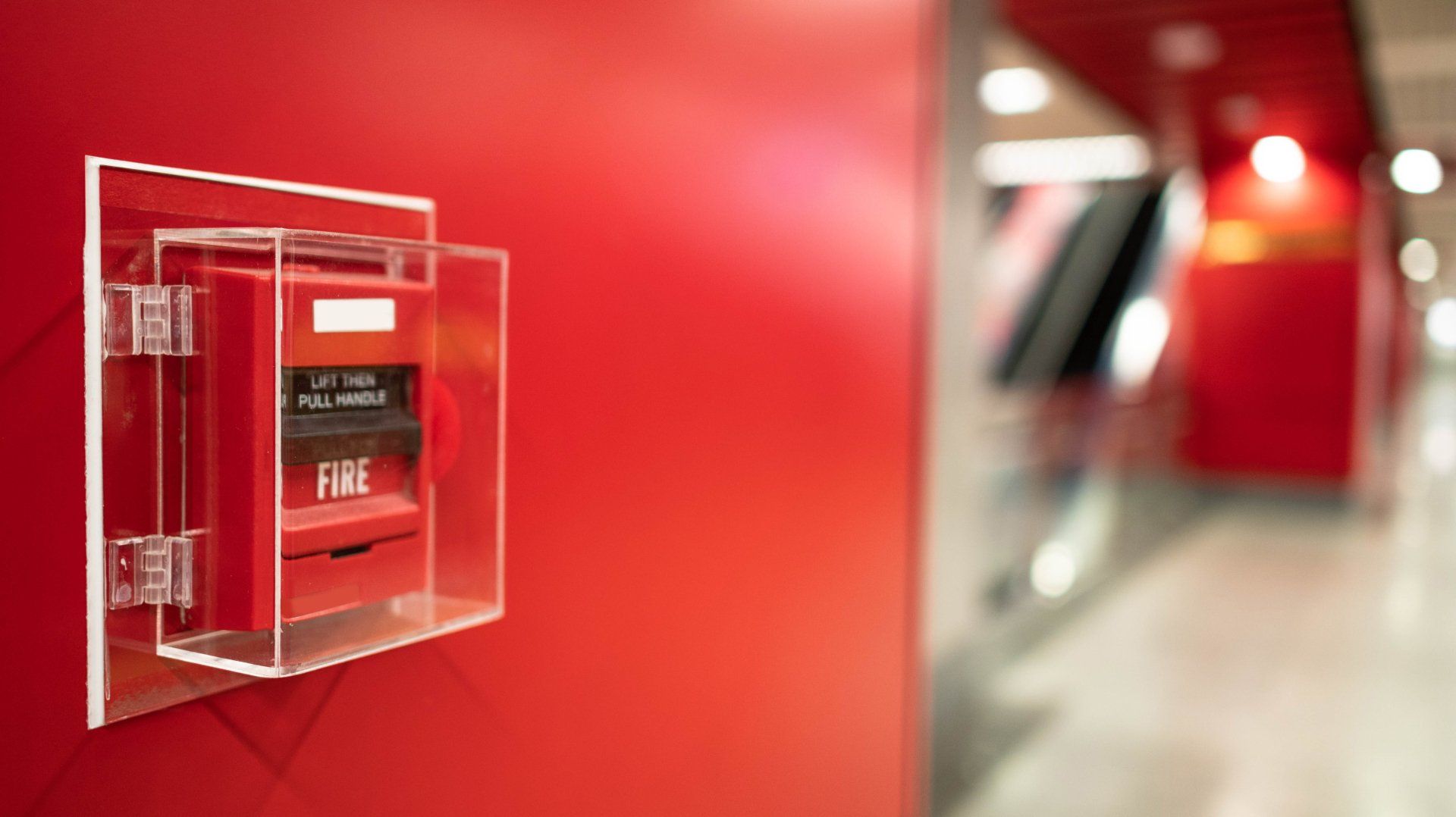 Une alarme incendie rouge est montée sur un mur rouge dans un couloir.