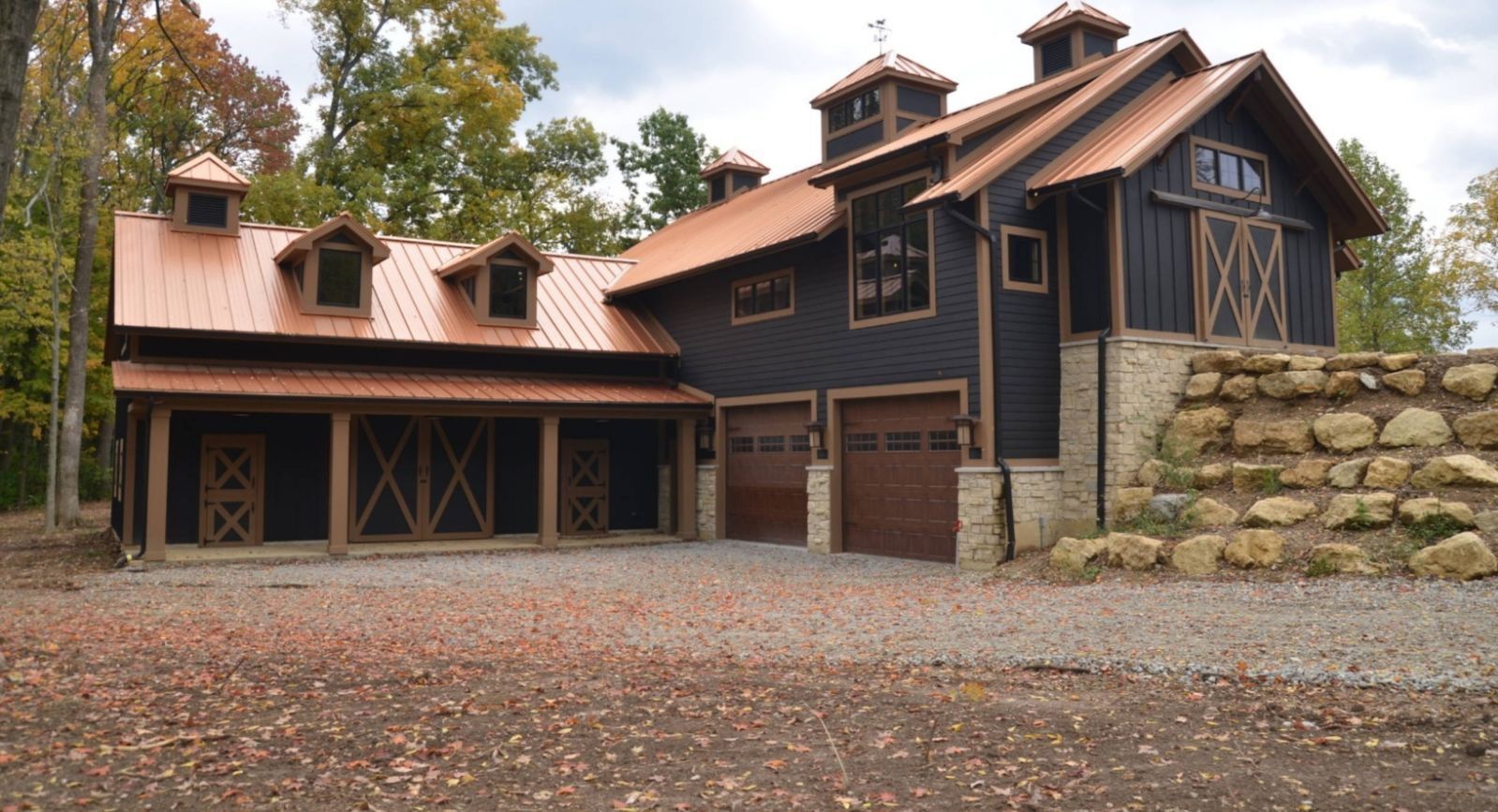 Barn-style building with copper roof, dark siding, stone accents, and three garage doors.