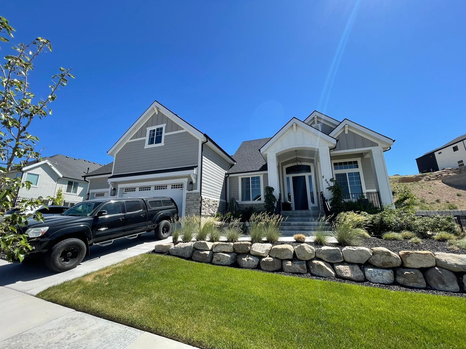 Suburban house with stone retaining wall, green lawn, and black SUV parked in the driveway under a blue sky