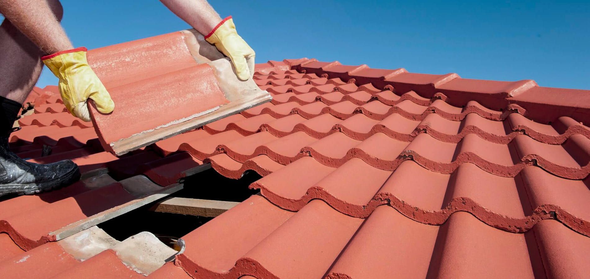 A person wearing gloves installing a red tile on a roof against a blue sky.